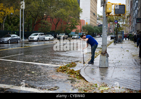 Un uomo che pulisce storm i detriti dai forti venti di uragano Sandy lontano da una tempesta scaricare visto in New York Foto Stock