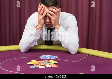 Uomo con testa in mani al tavolo del poker Foto Stock