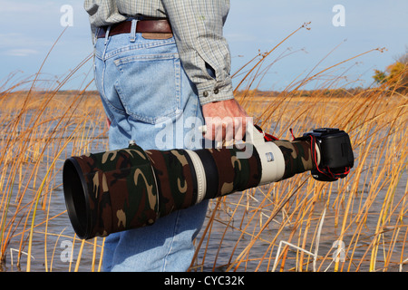 Fotografo professionista che porta un mimetizzata Canon super teleobiettivo e DSLR. Foto Stock