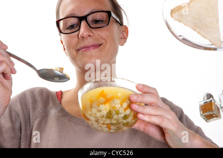 Giovane donna è seduta al tavolo di vetro, mangiare una zuppa di verdure, tagliatelle. Foto Stock