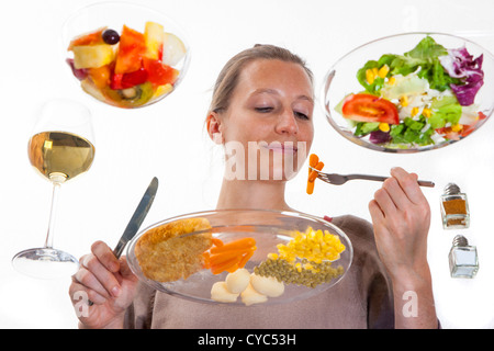 Giovane donna è seduta al tavolo di vetro. Mangiare un pasto, Schnitzel, patate, verdure, insalata mista, insalata di frutta, vino bianco. Foto Stock