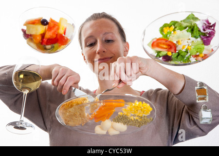 Giovane donna è seduta al tavolo di vetro. Mangiare un pasto, Schnitzel, patate, verdure, insalata mista, insalata di frutta, vino bianco. Foto Stock