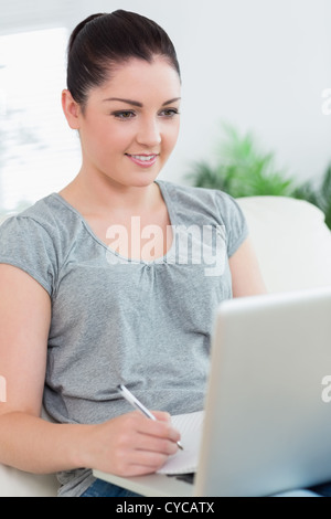 Giovane donna sul lettino usando un computer portatile e di prendere appunti Foto Stock
