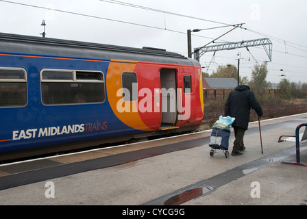 Uomo vecchio con bastone e con ruote carrello oltrepassando East Midlands treno fermato a Grantham Station Foto Stock