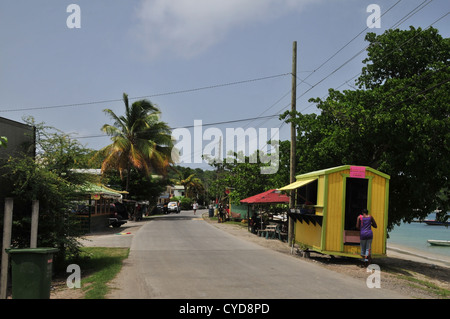 Blue sky view man walking road, legno verniciato di negozi che vendono frutta verdura, Harvey Vale, Tyrrel Bay, Carriacou, West Indies Foto Stock