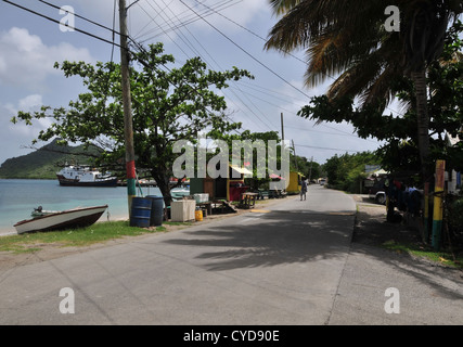 Blue sky view road, alberi, frutta ortaggi legno negozi, uomo di strada a piedi, barche, Harvey Vale, Tyrrel Bay, Carriacou, West Indies Foto Stock