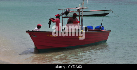 L uomo lo sterzo, uomo che sta tenendo il pesce, uomo in piedi sul mare rosso guida barca da pesca su Paradise Beach, Carriacou, West Indies Foto Stock