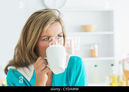 La donna in vestaglia seduta in cucina e bere Foto Stock