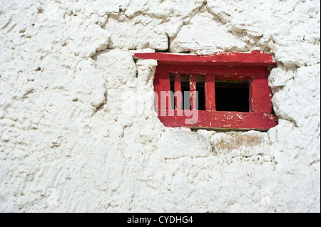 Vecchio rosso sul telaio di una finestra sul muro bianco al monastero buddista. India, Ladakh Leh, monastero di Shey Foto Stock