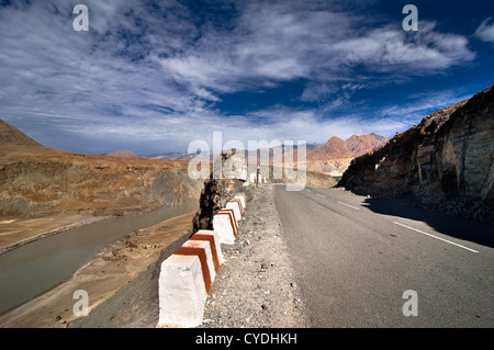 Strada attraversando Himalaya lungo il fiume Indo sotto blu cielo nuvoloso. India, Ladakh, altitudine 3300 m Foto Stock