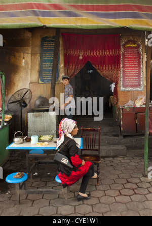 Giovane donna uigura in attesa al tavolo di un ristorante e cucinare, Keriya, Città Vecchia, Xinjiang Uyghur Regione autonoma, Cina Foto Stock