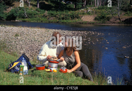 Giovane picknicking dal fiume sul fornello da campeggio, Grampians, Invernesshire, Scozia Foto Stock