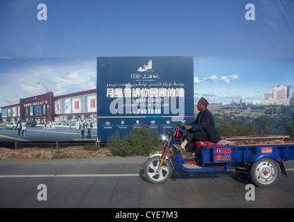 Il vecchio uomo passando di fronte la pubblicità per la nuova Immobiliare, Nuova città di Kashgar, Xinjiang Uyghur Regione autonoma, Cina Foto Stock