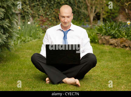 Imprenditore di successo in camicia bianca e cravatta lavoro zampe trasversale su un computer portatile in un giardino Foto Stock