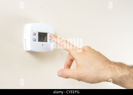 Mano cambiando la temperatura del termostato in una casa Foto Stock