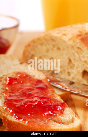 Pane appena sfornato con confettura di fragole spalmato su di esso con un bicchiere di succo di arancia. Foto Stock