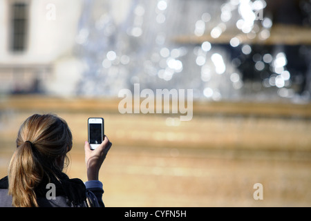 Vista posteriore di una giovane donna di prendere una fotografia in Trafalgar Square - parte di una fontana in background Foto Stock
