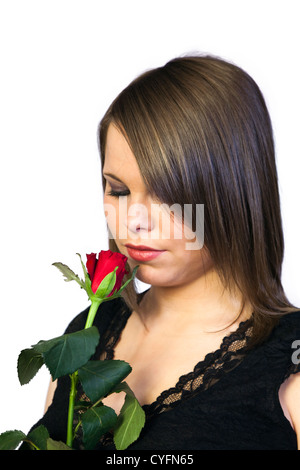 Ritratto di un bel giovane donna con i capelli scuri che indossa un top nero e odore di una rosa rossa su uno sfondo bianco Foto Stock