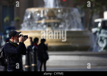Un maschio di scattare una fotografia in Trafalgar Square - un fuori fuoco fontana in background Foto Stock