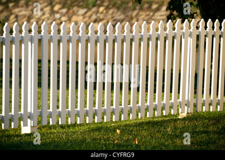 Un bianco di legno Picket Fence in un ben conservato cantiere durante il golden ora appena prima del tramonto su un inizio di giornata autunnale. Foto Stock