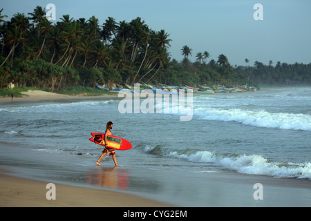 Viaggiare surfer entra nell'oceano per un surf a Weligama Bay in Sri Lanka Foto Stock