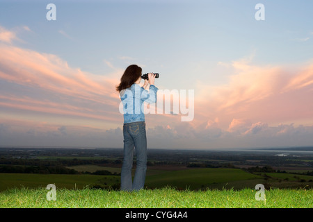 Donna che utilizza un binocolo guardando verso il canale inglese attraverso la campagna Foto Stock