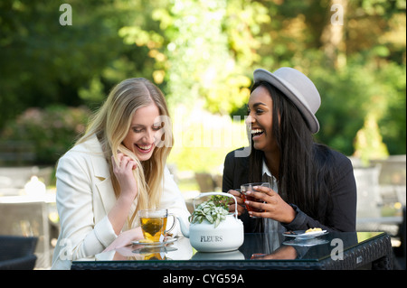 Due amiche della seduta in un ristorante esterno avente una buona volta mentre bevendo una tazza di tè Foto Stock