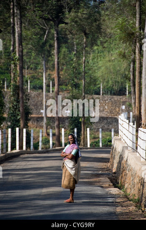Ritratto verticale di una signora indiana in trasandato abiti da lavoro in piedi sorridente in strada in una piantagione di tè in India. Foto Stock