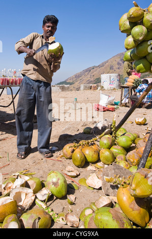 Ritratto verticale di un uomo indiano la preparazione di noci di cocco da bere con un machete in corrispondenza di un bordo strada stallo in Kerala. Foto Stock