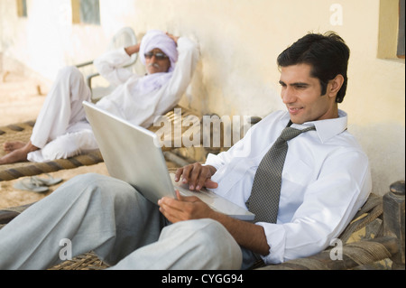 Imprenditore utilizzando un computer portatile con il suo padre sdraiato su un lettino in background Foto Stock