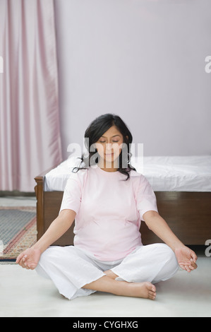 Donna incinta meditando in camera da letto Foto Stock