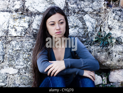 Premuto e solitaria ragazza adolescente, triste espressione faccia appoggiata sulla parete di pietra. Foto Stock