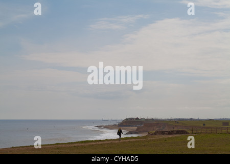 Il camminatore solitario sulla scogliera. Happisburgh beach e costa. Difesa del Mare rock inguine sull orizzonte. Guardando a sud dal parcheggio pubblico.Norfolk. East Anglia. Foto Stock