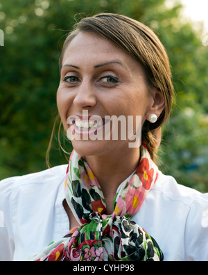 Sorridente giovane donna che indossa una camicia bianca e una sciarpa colorata contro uno sfondo verde. Foto Stock