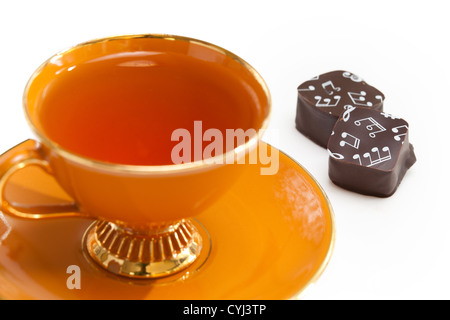 Orange tazza da tè a tea party con nota musicale di cioccolato con banconote stampate su di essi. Foto Stock