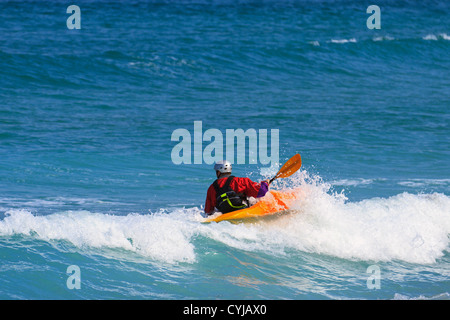 Uomo in un bianco acqua kayak singolo indossando una capote asciutta e casco come cavalca l'onda Foto Stock