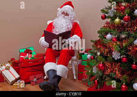 Babbo Natale seduto su una sedia a dondolo la lettura della 'naughty o bell' elenco circondato da regalo presenta. Foto Stock