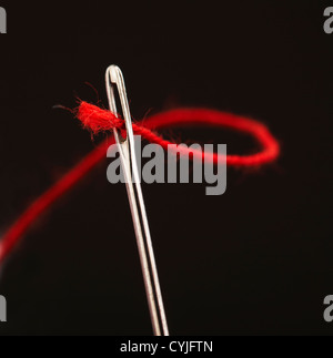 Filo rosso che passa attraverso gli occhi di ago, primo piano Foto Stock