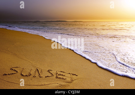 La parola tramonto è scritto a mano in sabbia vicino al mare in una spiaggia al tramonto Foto Stock