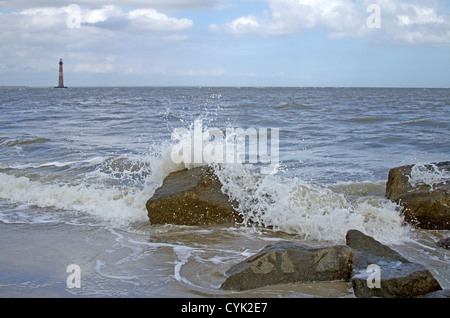 Morris il faro in distanza con la rottura del mare sulle rocce in primo piano nei pressi di follia Beach, Carolina del Sud, STATI UNITI D'AMERICA Foto Stock