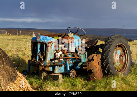 Un arrugginimento vecchio trattore blu sorge in un campo vicino al mare Foto Stock