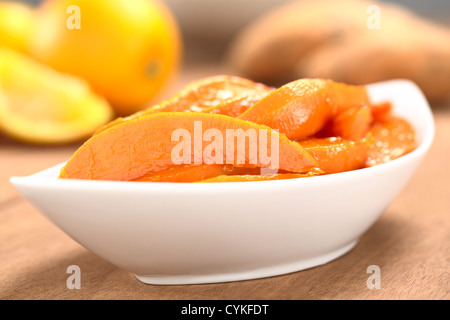 Ciotola di patata dolce caramellato cunei con lo zucchero di canna e il succo d'arancia fresco con patate dolci e arance nel retro Foto Stock