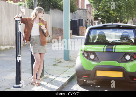 Donna ricarica auto elettrica su strada Foto Stock