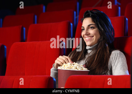 Film divertente: ritratto di una bella ragazza in un teatro vuoto, lei mangia popcorn e sorrisi Foto Stock