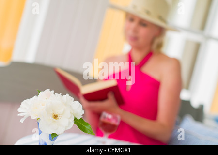 Signora legge un libro sulla veranda, reposeful atmosfera, formato orizzonte, stretta di concentrarsi sul fiore Foto Stock