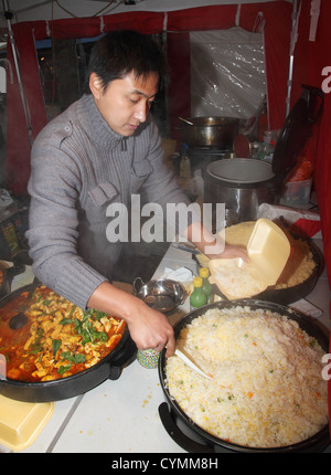 Uomo di aspetto Asiatico che serve il riso all'interno di una stalla in York mercato aperto, England Regno Unito Foto Stock