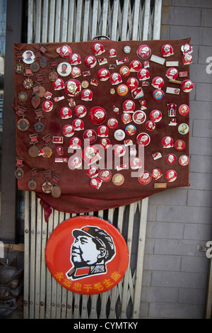 Insegne comunista e i badge con il Presidente Mao sul visualizzatore in corrispondenza di un negozio in una strada di Liulichang, Pechino, Cina. Foto Stock