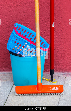 Blue secchio di plastica e vestiti cestello con un pavimento di colore arancione spazzola contro una parete rossa Foto Stock