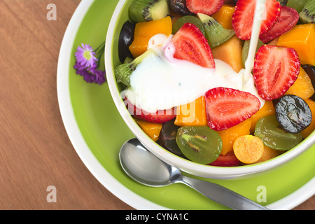 Fresca e sana insalata di frutta con fragole, kiwi, uva, mango e physalis in una ciotola con lo yogurt è versato sopra Foto Stock