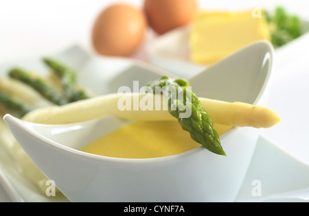 Gli asparagi giacente su una ciotola piena di salsa olandese (molto leggera profondità di campo, messa a fuoco sulla testa dell'asparago verde) Foto Stock